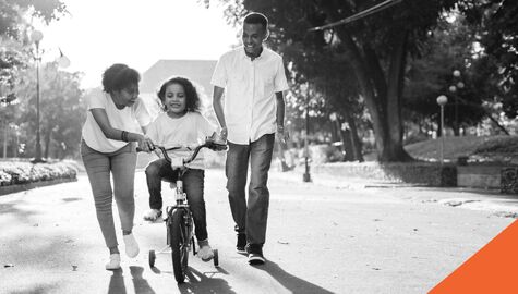 Parents teaching their daughter how to ride a tricycle.