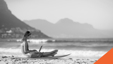 Work from Anywhere | Destinations for your next workation | Billyard Insurance Group | woman sitting on a beach with laptop with mountains in the background.